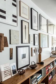 there are many framed pictures on the wall above the bookshelf in this living room