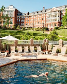 a man swimming in a pool with chairs around it and an apartment building behind him