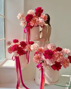 a woman standing next to three vases with flowers in them and ribbons on the sides