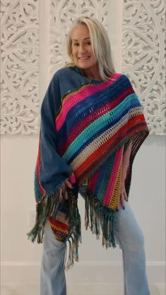 a woman standing in front of a white wall wearing a multicolored shawl