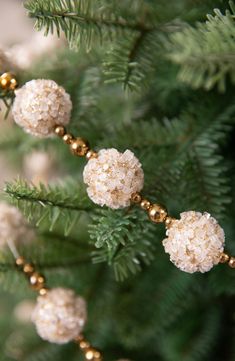 some white balls are hanging from a christmas tree branch with gold bead trimmings