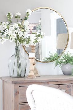 a mirror and vase with flowers on a dresser