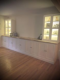 an empty room with white cabinets and wood flooring is pictured in this image, there are two windows above the counter