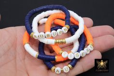 Navy Blue, Orange, White, and Gold Bracelets in Heishi Beads by Regina Harp Designs These bracelets are in a Navy Blue, Soft Orange, White, and Gold colors with your choice of bracelet style. They can be made with our other bead colors as well; message us if you would like to customize your bracelet. If you need a smaller or extra large size in the bracelet, please leave us a note with your order. NOTE: Last picture shows in a dark orange. If you prefer that color, please leave us a note. **SPEC Clay Beaded Bracelets, Tiger Team, Halloween Bracelet, Blue Orange White, Soft Orange, White Jewelry Box, Clay Bracelet, Diy Bracelet Designs, Beads Bracelet Design