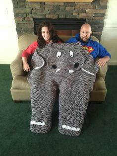 a man and woman sitting on a couch holding up an elephant crocheted blanket