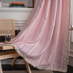 a pink curtain hanging from the side of a wooden chair next to a table with a lamp on it