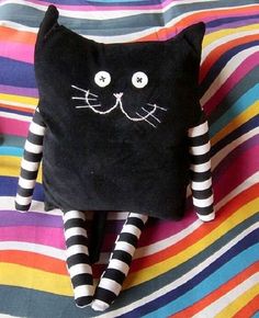 a black cat stuffed animal laying on top of a colorful striped bed sheet with white and black stripes