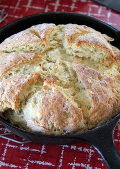 a skillet filled with bread on top of a red and white table cloth next to a knife