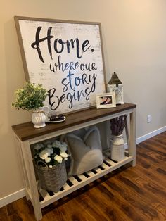 a sign that says home where our story begins on the wall above a shelf with flowers