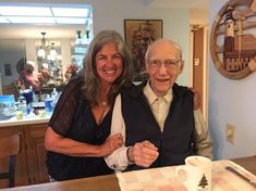 an older man and woman standing next to each other in front of a wooden table