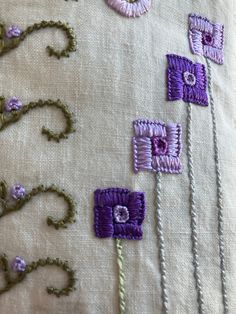 some purple and white flowers are on a pillow with beadwork around it's edges