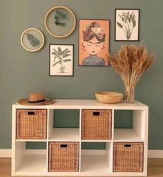 a white shelf with baskets and pictures on the wall