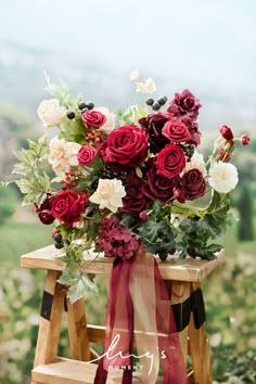 a bouquet of red and white flowers sitting on top of a wooden step stool with a ribbon tied around it