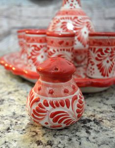 a red and white vase sitting on top of a counter next to other bowls, cups and saucers