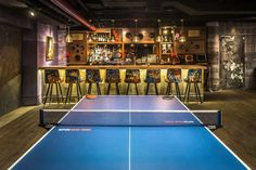 an indoor ping pong table with bar stools in the background and several chairs around it