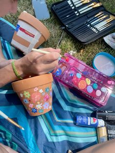 a person sitting on the grass painting with paintbrushes and other items in front of them