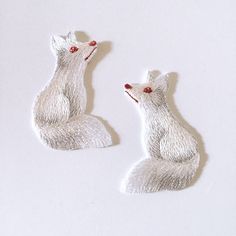 two embroidered white foxes sitting next to each other