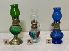 three different colored glass vases sitting next to each other on top of a table