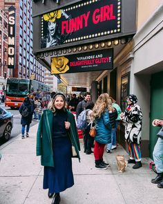 a woman walking down the street in front of a funny girl theater