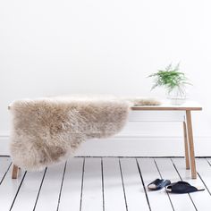 a bench with a fur on it next to shoes and a plant in a vase