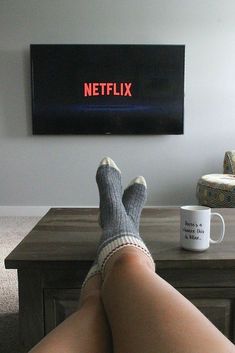 a person with their feet up on a table in front of a television that reads netflix