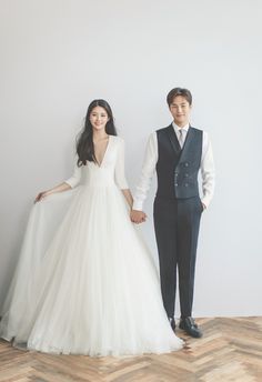 two people standing next to each other in front of a white wall wearing wedding dresses