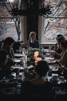 a group of people sitting around a dinner table with candles in front of the window