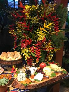 a table topped with lots of different types of cheeses and fruit next to flowers