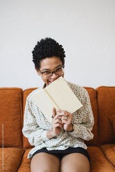 a woman sitting on top of a couch holding an open book in her hands and smiling at the camera