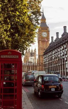 a red telephone booth sitting on the side of a road next to a tall clock tower