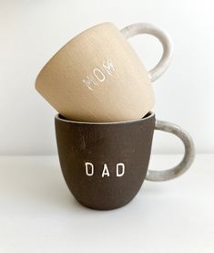 two coffee mugs with the words mom and dad printed on them are stacked next to each other