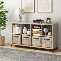 a living room with some baskets on top of the shelf and pictures hanging above it