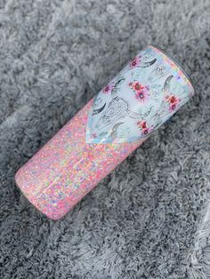 a pink and blue tube with glitter on it sitting on a gray carpet next to a cell phone