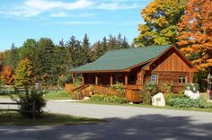 a log cabin sits on the side of a road in front of trees with fall foliage