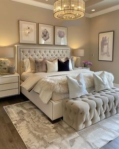 a large white bed sitting in a bedroom on top of a hard wood floor next to a chandelier