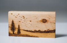 a wooden block with trees and birds flying over the horizon, on a white surface