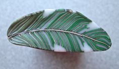 a green and white leaf shaped broochle sitting on top of a gray surface