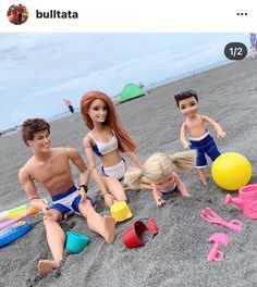 three dolls are sitting on the beach with toys in front of them and one is wearing a bathing suit