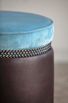 a blue ottoman sitting on top of a wooden floor next to a brown stool with studded trim