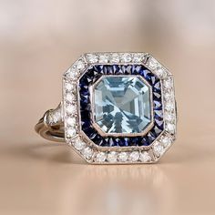 This platinum ring features a 1.97 carat aquamarine in an Asscher cut. It is surrounded by a halo of calibrated French cut sapphires, as well as a second halo of round brilliant cut diamonds. Additional round brilliant cut diamonds adorn the shoulders. The total weight of the diamonds is approximately 0.51 carats. This ring is embellished with fine milgrain and an open-work under-gallery.
The approximate dimensions of the aquamarine are 8.00mm x 8.00mm. The measurements of this ring are approxim Diamond Ring With Halo, Ring With Halo, Asscher Cut Ring, Estate Diamond Jewelry, Vintage Inspired Rings, Aquamarine Engagement Ring, French Cut, Jun 2023, Engagement Ring Diamond