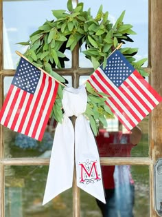 a wreath with two american flags hanging from it's side on a window sill