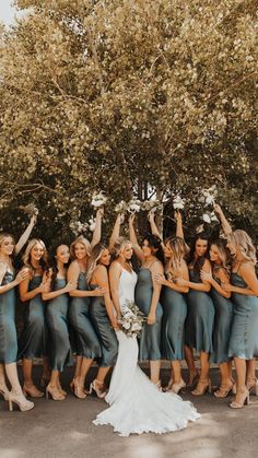 a group of women standing next to each other in front of a tree with their hands up