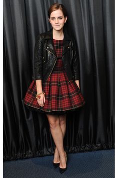 a woman standing in front of a black curtain wearing a red and black plaid dress