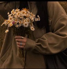 a woman holding a bouquet of daisies in her hands while wearing a brown coat