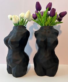 two black vases with white and purple flowers in them