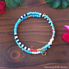 two bracelets with beads and charms on a wooden table next to pink flower petals