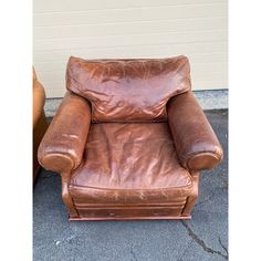 a brown leather chair sitting on top of a cement floor next to a white wall