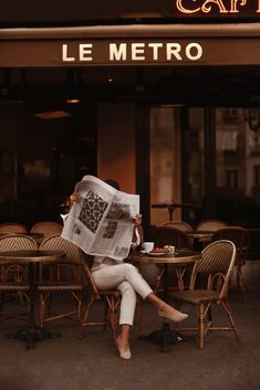 a woman sitting at a table reading a newspaper