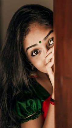 a woman with long dark hair and green eyes is peeking out from behind a wooden door