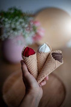 two crocheted ice cream cones with red and white toppings on them, held in someone's hand